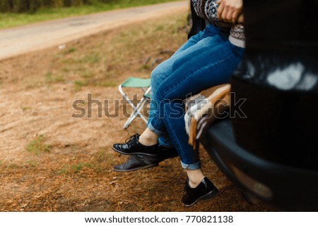 Closeup of feet of a happy traveler couple sitting in the car to open the trunk and watch the sunrise in the forest. Young couple hugging sitting in the trunk and chatted feet in the Park outdoors.
