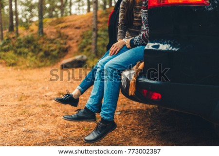 Closeup of feet of a happy traveler couple sitting in the car to open the trunk and watch the sunrise in the forest. Young couple hugging sitting in the trunk and chatted feet. Stylish toned photo.