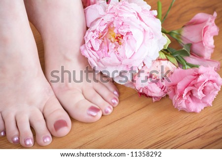 close-up of woman?s feet with pink nail polish and fresh pink flowers on wooden floor