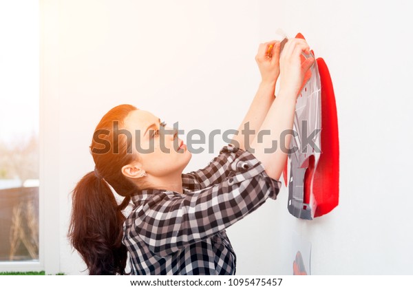 A close-up\
of a female artist draws a picture of a car and draws it in red on\
a white wall in the children\'s\
room