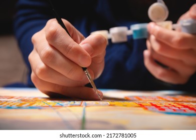 Close-up Of A Female Artist's Hand Painting With Watercolors Color On Canvas With A Brush In A Dark Modern Art Studio. The Concept Of A Young Artist Or Female Artist.