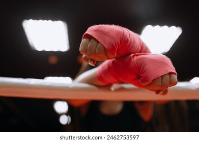 Close-up of a female boxer in pink sports protective armbands preparing for a tough fight. Hands with bandages on the ropes of the boxing ring - Powered by Shutterstock