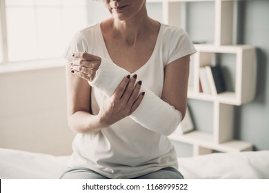 Nahaufnahme des gebrochenen Arms von Frauen in der Plakatdose. Kaukasische verletzte Frau in weißem T-Shirt Sitting und Halten Handgelenk in Gypsum Bandage mit physischem Schmerz in zersplittertem Knochen. Konzept der Gesundheitsversorgung