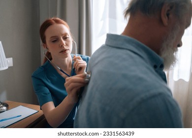 Close-up of female cardiologist doctor examining lungs of elderly senior male patient at home using stethoscope. Nurse listening with stethoscope to back of mature adult man in hospital room. - Powered by Shutterstock