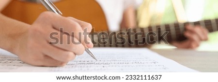 Close-up of female composer writing music notes in notebook. Musician composes music while sitting with guitar.