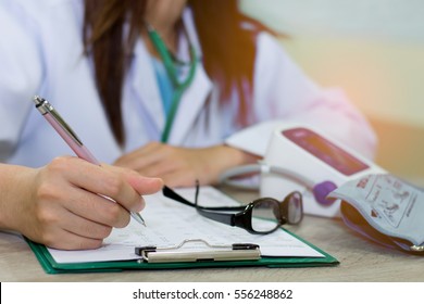 Close-up of a female doctor in office filling out application form with smartphone , sitting at the table in the hospital - Powered by Shutterstock