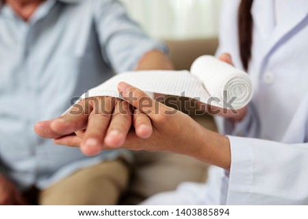 Close-up of female doctor putting a bandage on injured hand of senior man at hospital