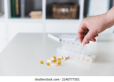 Closeup of female elderly hands sorting pills. Medical pill box with doses of tablets for daily take with white, yellow, beige drugs and capsules. Young woman getting her daily vitamins at home