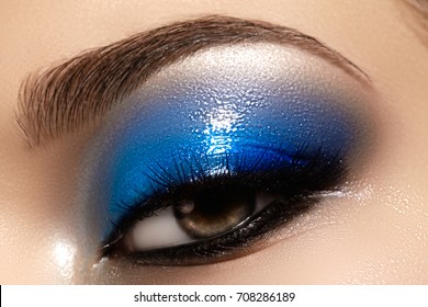 Closeup female eye with beautiful fashion bright make-up. Beautiful shiny blue eyeshadow, wet glitter, black eyeliner, perfect eyebrows shape.