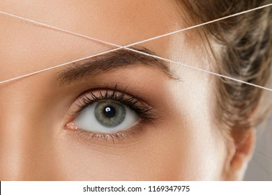 Close-up Of Female Eye With A Thread. Eyebrow Threading - Epilation Procedure For Brow Shape Correction