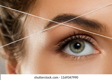 Close-up of female eye with a thread. Eyebrow threading - epilation procedure for brow shape correction