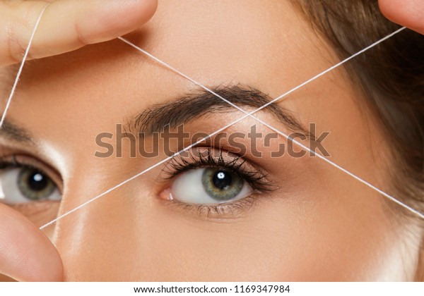 Close-up of female\
eye with a thread. Eyebrow threading - epilation procedure for brow\
shape correction