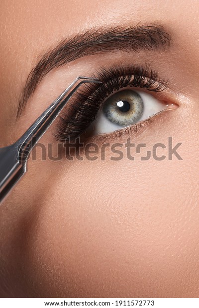 Closeup of female eye and tweezers during eyelash\
extension 