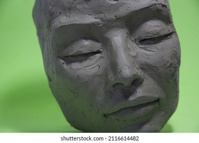 Close-up of female face in clay. Sculpture on green background: Artwork in process of creation. - Shutterstock ID 2116614482
