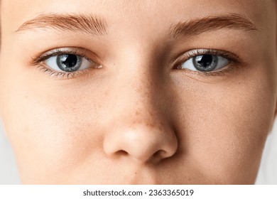 Close-up of female face, eyes, nose. Beautiful young woman with freckles on nose and blue eyes. Concept of skin care, natural beauty, cosmetology and cosmetics, spa