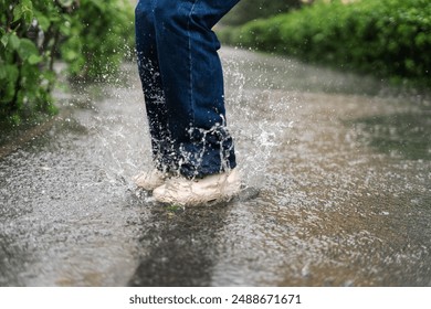 Closeup female feet in boots jumping in puddle during the rain at green city park. Carefree lifestyle and people concept  - Powered by Shutterstock