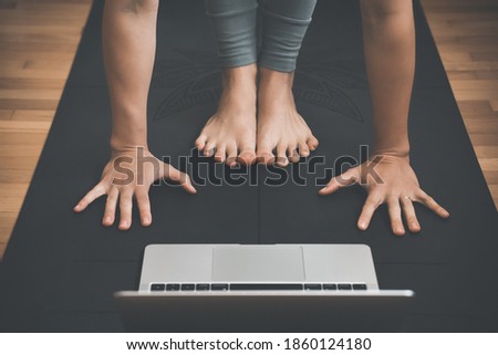 Closeup of female feet and palms on yoga mat with laptop. People practicing yoga online. Concept of video training class on digital devices.