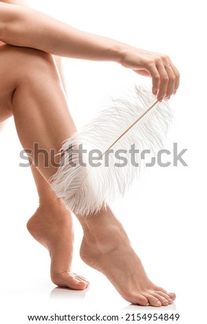 Closeup of female feet with smooth skin and soft ostrich feather on white background