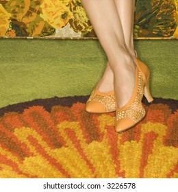 Close-up of female feet wearing orange shoes against colorful retro rug.