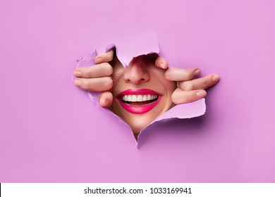 close-up of female fingers, nose and lips with pink lipstick and a broad smile that peeps through purple grapesafed paper