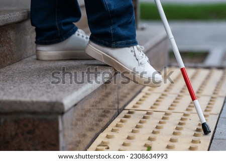 Close-up of female foot, walking stick and tactile tiles. Blind woman walking down stairs using a cane. 