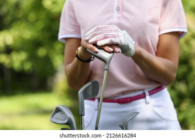 Close-up of female golf player holding putter and wearing protective gloves. Professional sportswoman in luxury private club. Active lifestyle and winner concept