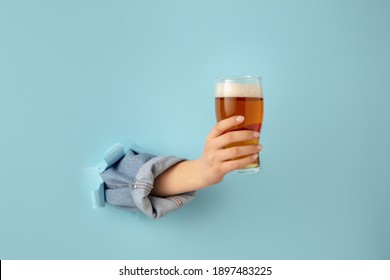 Close-up female hand with beer breaks through blue paper background. - Powered by Shutterstock