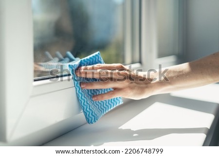 closeup of female hand with blue rag wipe window sill and plastic frame from dust at office. cleaning service concept