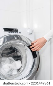 Closeup Of Female Hand Closing Door In Automatic Washing Machine With Dirty Clothes Or Bath Towel In White Bathroom. Household Appliance, Housekeeping Concepts