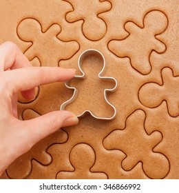 Closeup of female hand with cutter making homemade traditional gingerbread men Christmas cookies. Above view