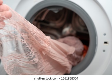 Close-up. Female Hand Holding A Pink Lace Dress Just Washed In An Automatic Washing Machine, Delicate Wash Mode 