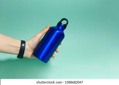 Close-up Of Female Hand Holding A Reusable, Aluminium Thermal Water Bottle Of Phantom Blue Color, Isolated On Aqua Menthe Background.