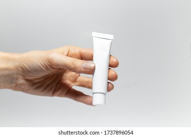 Close-up Of Female Hand Holding Toothpaste Tube On Studio Background Of White.