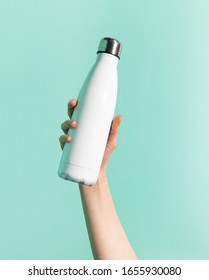 Close-up of female hand holding white reusable steel stainless thermo water bottle isolated on background of cyan, aqua menthe color. Plastic free. - Shutterstock ID 1655930080