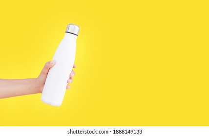 Close-up Of Female Hand Holding White Reusable Steel Thermo Water Bottle Isolated On Background Of Yellow Color With Copy Space.