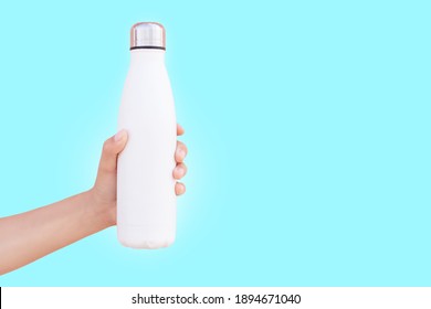 Close-up Of Female Hand Holding White Reusable Steel Thermo Water Bottle Isolated On Background Of Cyan Color With Copy Space.