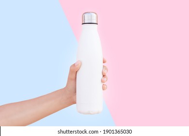 Close-up of female hand holding white reusable steel thermo water bottle isolated on two backgrounds of blue and pink colors.