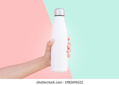 Close-up of female hand holding white reusable steel thermo water bottle isolated on two background of red and green colors. - Shutterstock ID 1982696522