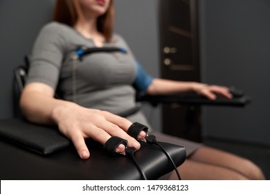 Closeup of female hand with indicators measuring pulse during lie detector test. Sincere woman in grey dress sitting in chair and answering questions. Concept of examination and inquiry. - Shutterstock ID 1479368123
