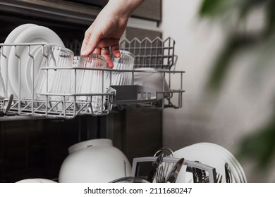 Close-up of female hand loading dished to, empty out or unloading from open automatic stainless built-in dishwasher machine with clean utensils inside in modern home kitchen. Household domestic life - Shutterstock ID 2111680247