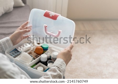 Closeup female hand neatly placing medicament at domestic first aid kit top view. Storage organization in transparent plastic box drug, pill, syringe, bandage. Fast health help safety emergency supply