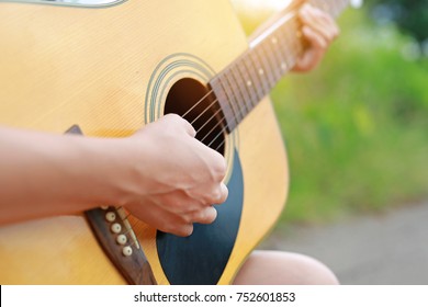 Close-up female hand playing on acoustic guitar outdoor.