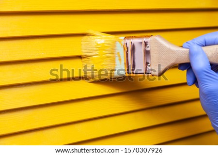 Closeup female hand in purple rubber glove with paintbrush painting natural wooden door with orange paint. Concept colored bright creative design interior for young family. How to Paint Wooden Surface