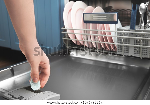 Close-up female hand putting tablet in dishwasher\
detergent box