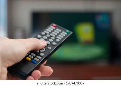 Closeup of female hand with the remote control of television, pressing buttons. Thumb pressing button, blurred cartoon on background. Woman watching TV at home and using controller. 