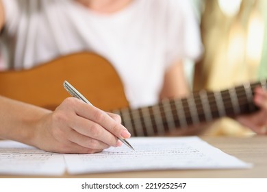 Close-up Of Female Hand Writing Notes Of New Song. New Ideas Inspirational Singer Composing Music With Guitar At Home. Music Art Concept