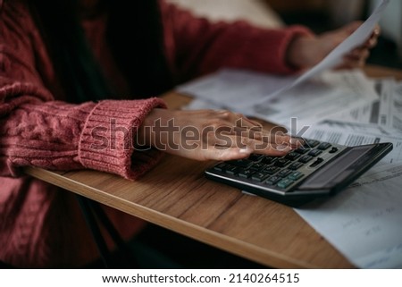 Close-up female hands with a calculator and abacus in the living room at home. A young woman calculates monthly household expenses, taxes, bank account balance and credit card bill payments.