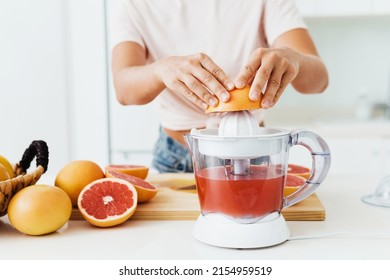Closeup of female hands and citrus juicer during fresh grapefruit juice preparation