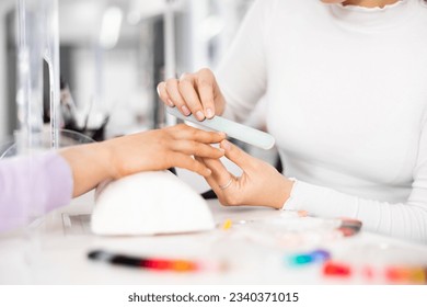 Closeup of female hands during professional manicure in beauty parlor. Manicurist shaping nails to client with nail file.. - Powered by Shutterstock