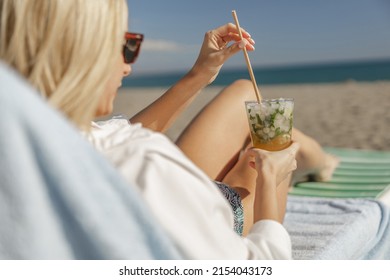 Closeup Of Female Hands Holding Cocktail Glass, Sitting On A Deck Chair